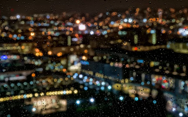 A beautifully blurred cityscape glistens with colorful lights, as raindrops adorn the window, creating a serene and atmospheric HD desktop wallpaper.