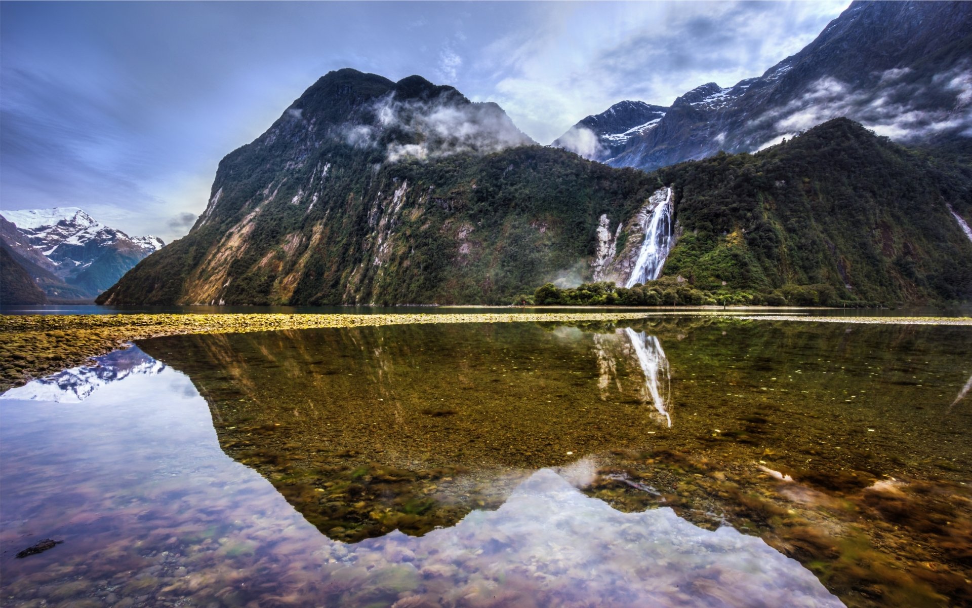 HD nature desktop wallpaper showing a mountain landscape with a waterfall reflected clearly in still water under a cloudy sky.