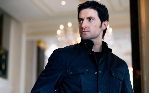 Dark-haired man in a navy jacket stands in an elegant, chandelier-lit interior, gazing to the side — 2K Quad HD PC desktop wallpaper.