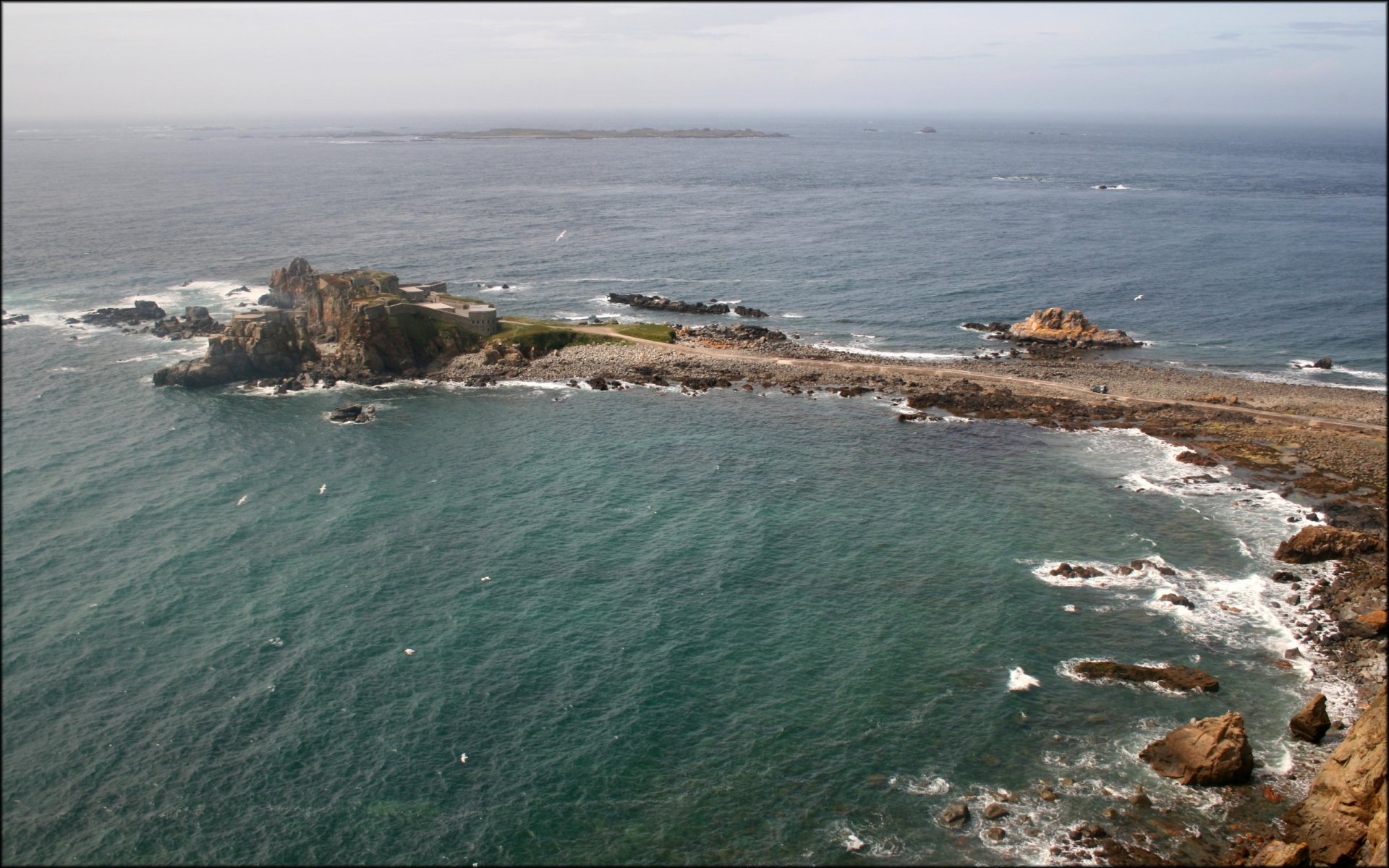 A stunning aerial view of Fort Clonque, showcasing rugged coastal landscapes and clear blue waters. This HD desktop wallpaper captures the beauty of man-made structures in nature.
