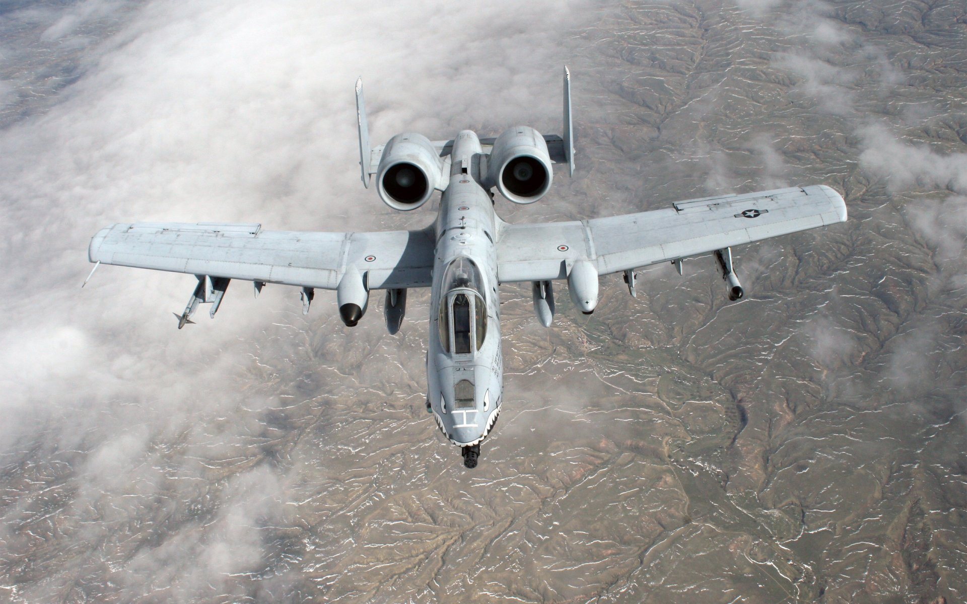 A Fairchild Republic A-10 Thunderbolt II military airplane flying above a rugged landscape, captured in HD for a desktop wallpaper background.