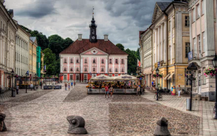 2K Quad HD PC desktop wallpaper of Tartu’s cobblestone town square, showcasing man-made historic architecture: the pink town hall, flanked by classical buildings, market stalls and an overcast sky.