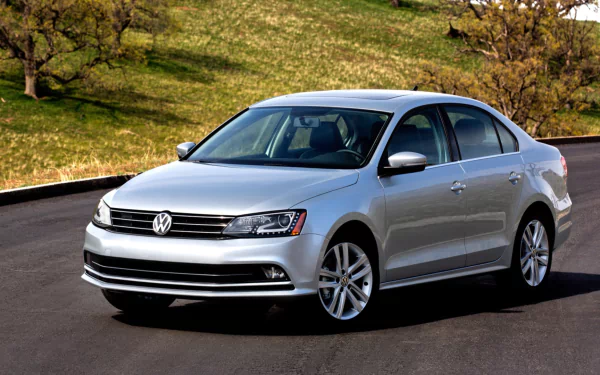 Silver Volkswagen Jetta sedan on a paved road with grassy hills in the background — HD PC desktop wallpaper and background.