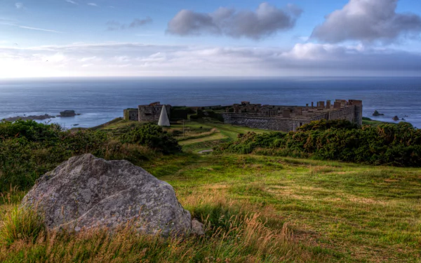 HD desktop wallpaper of Fort Tourgis, a man-made coastal fortification surrounded by grassy fields under a cloudy sky.