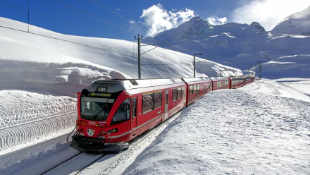A striking RhB train glides through a snow-covered landscape in Switzerland, framed by majestic mountains, creating a captivating HD wallpaper background.