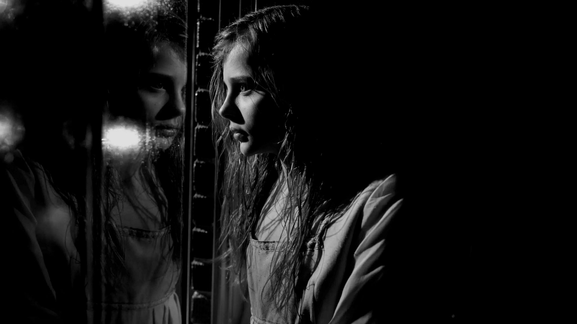 A moody black-and-white image from the movie *Let Me In*, featuring a young girl gazing into a reflective surface, creating an atmosphere of mystery and intrigue.