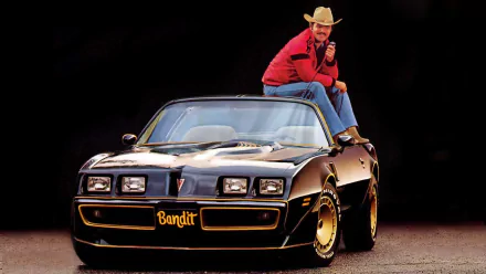 HD PC desktop wallpaper featuring the movie Smokey and the Bandit with the Bandit character sitting on a black Trans Am car against a dark background.