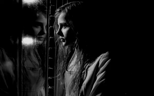 A moody black-and-white image from the movie *Let Me In*, featuring a young girl gazing into a reflective surface, creating an atmosphere of mystery and intrigue.