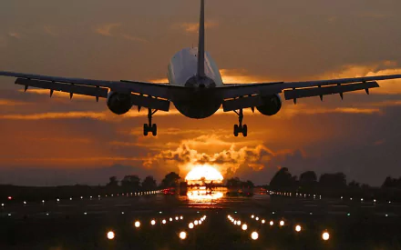 A Boeing 767 airplane landing at sunset, captured in an HD desktop wallpaper showcasing the aircraft and runway lights against an orange sky.