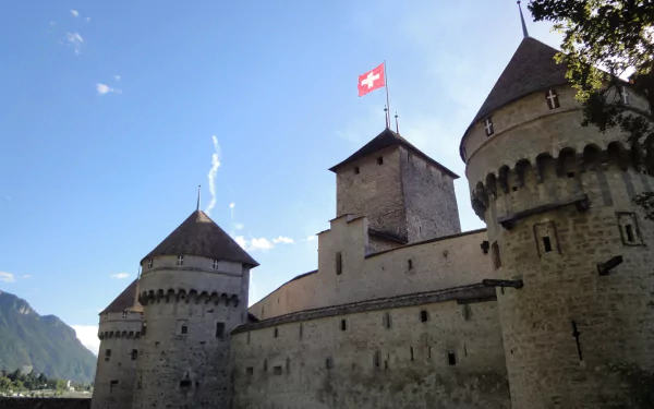 Château de Chillon, Veytaux, Switzerland — man made medieval lakeside castle with towers and Swiss flag against a blue sky; HD PC desktop wallpaper/background.