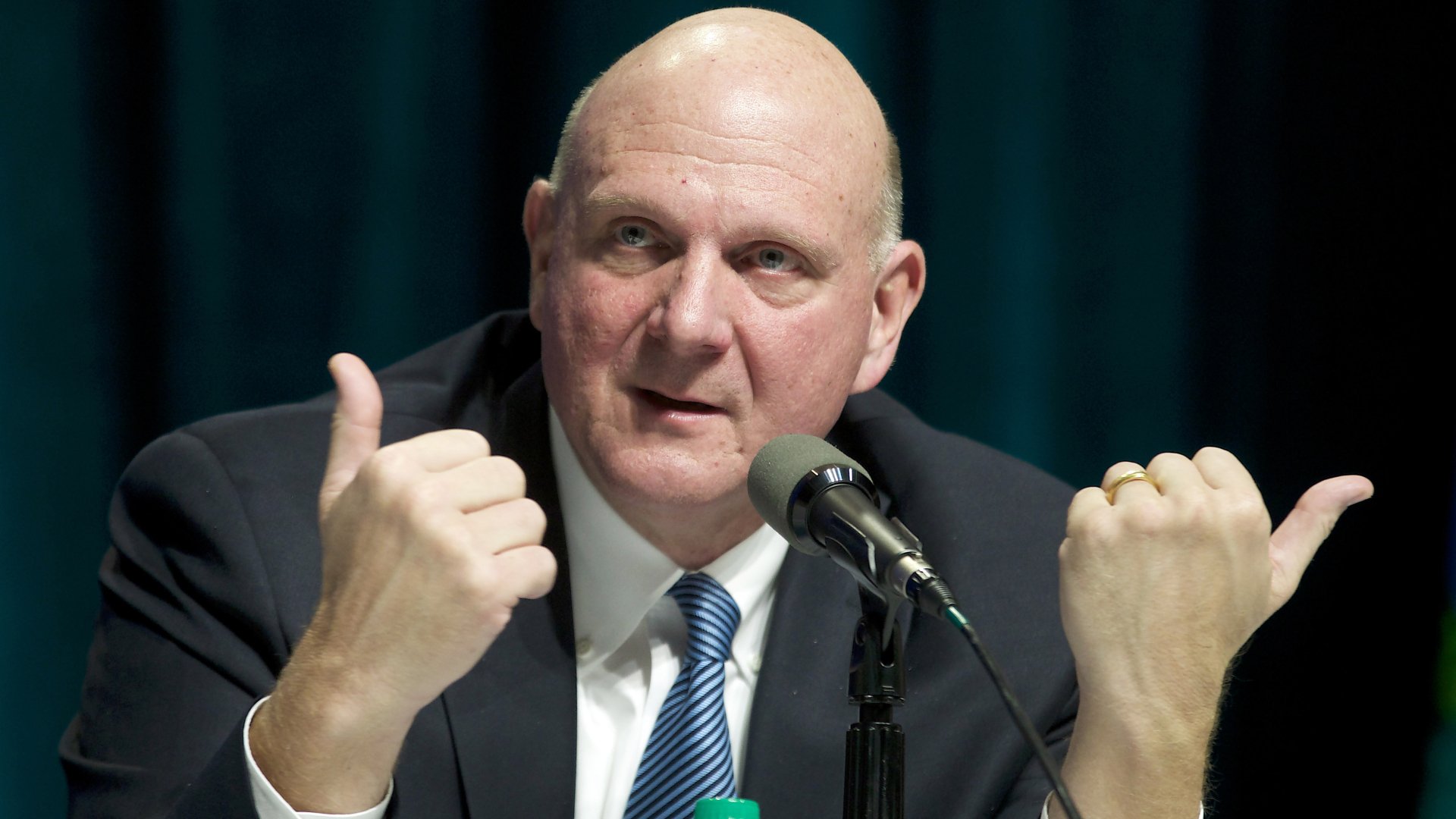 HD wallpaper featuring a man giving a thumbs-up gesture at a speaking event, serving as a dynamic desktop background.