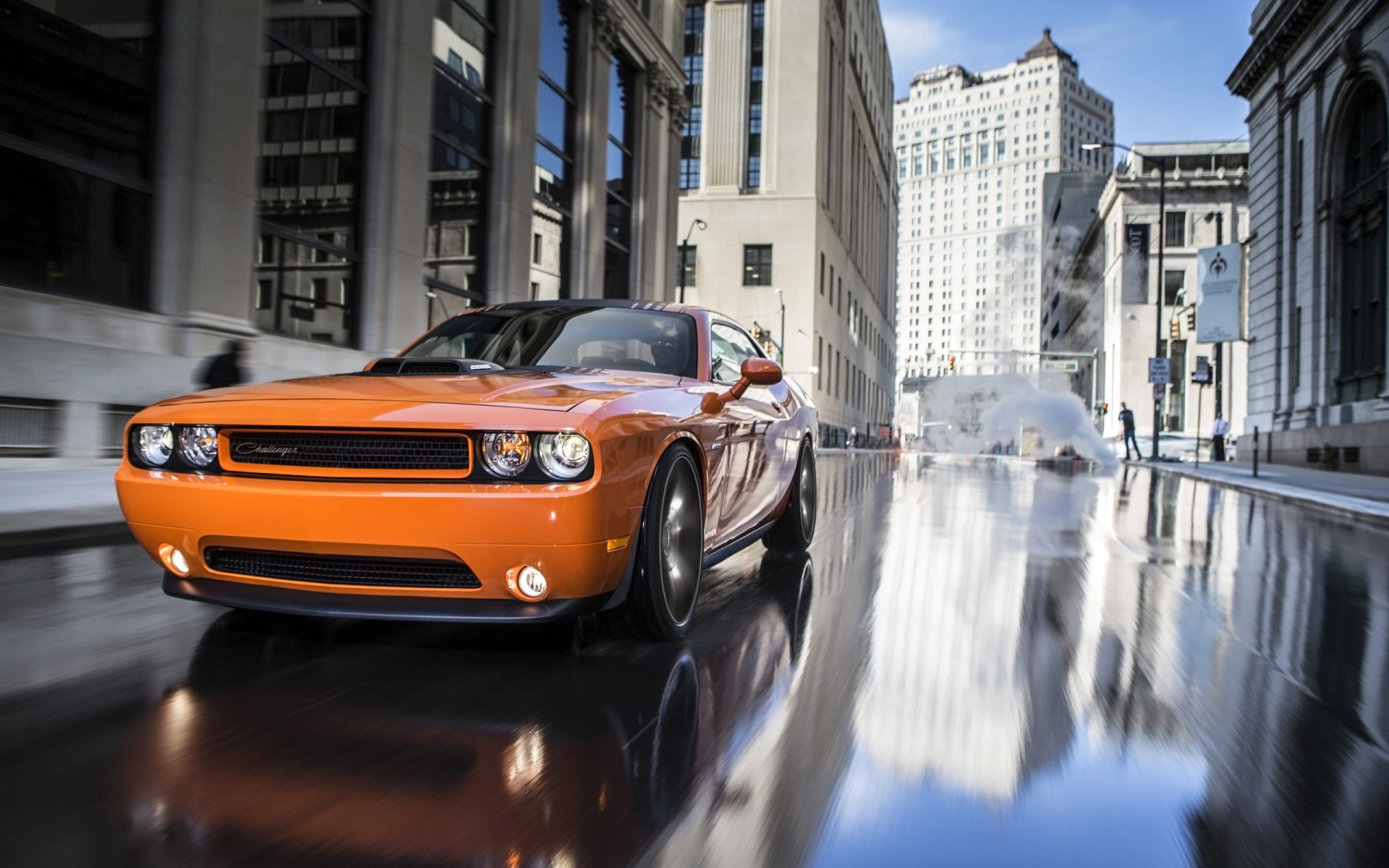 Orange Dodge Challenger RT Shaker driving on a wet city street with glossy reflections — 2K Quad HD PC desktop wallpaper/background.