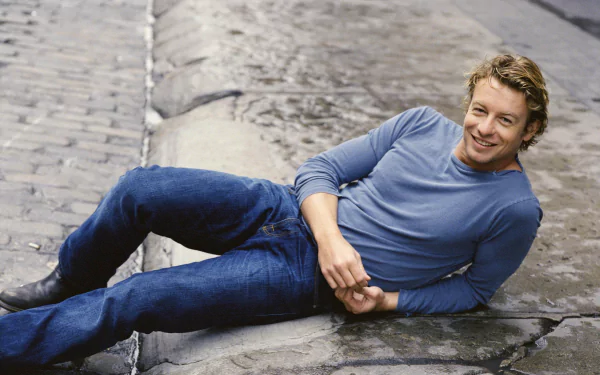 2K Quad HD desktop wallpaper of an Australian actor/celebrity reclining on cobbled pavement in a blue shirt and jeans, smiling toward the camera.
