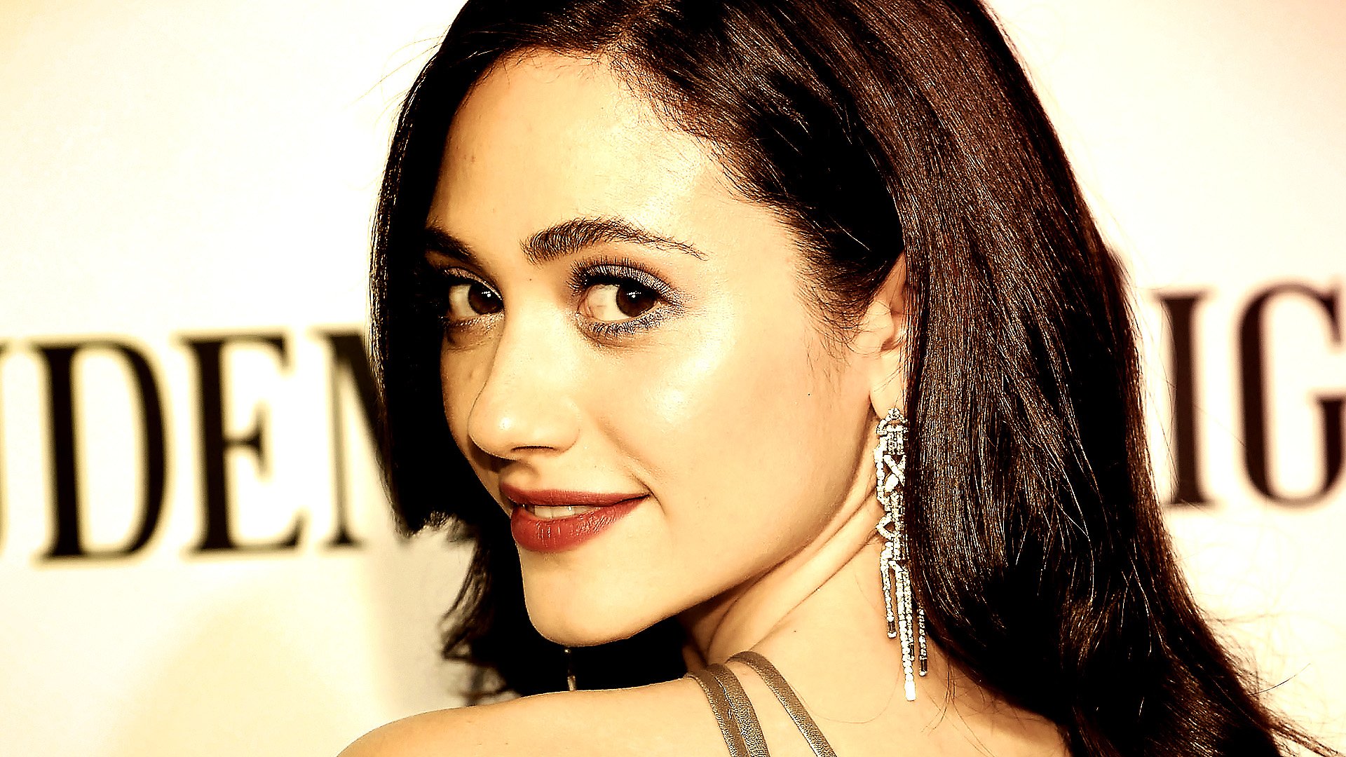 HD desktop wallpaper featuring a close-up portrait of celebrity Emmy Rossum with glowing skin and long dark hair, wearing a dangling earring.