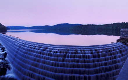 A serene view of a man-made dam, showcasing a cascading waterfall against a tranquil lake, surrounded by rolling hills under a soft twilight sky. High-definition desktop wallpaper.