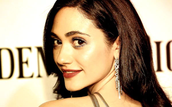 HD desktop wallpaper featuring a close-up portrait of celebrity Emmy Rossum with glowing skin and long dark hair, wearing a dangling earring.
