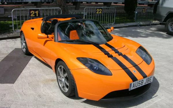 HD wallpaper of an orange Tesla Roadster with black stripes, parked outdoors.