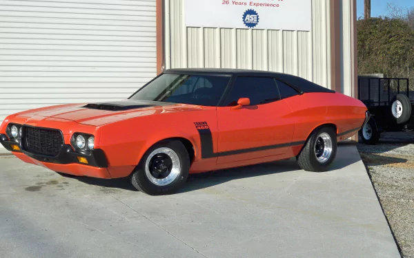 4K Ultra HD PC desktop wallpaper of an orange Ford Gran Torino Sport vehicle parked by a garage, showcasing the classic 1970s muscle car profile and black hood stripe.