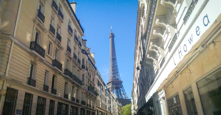 HD wallpaper of a Paris street with the Eiffel Tower in view, framed by city buildings under a clear sky.