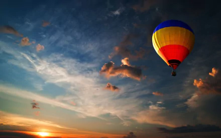 HD desktop wallpaper showing a colorful hot air balloon floating over a scenic sunset sky with clouds.