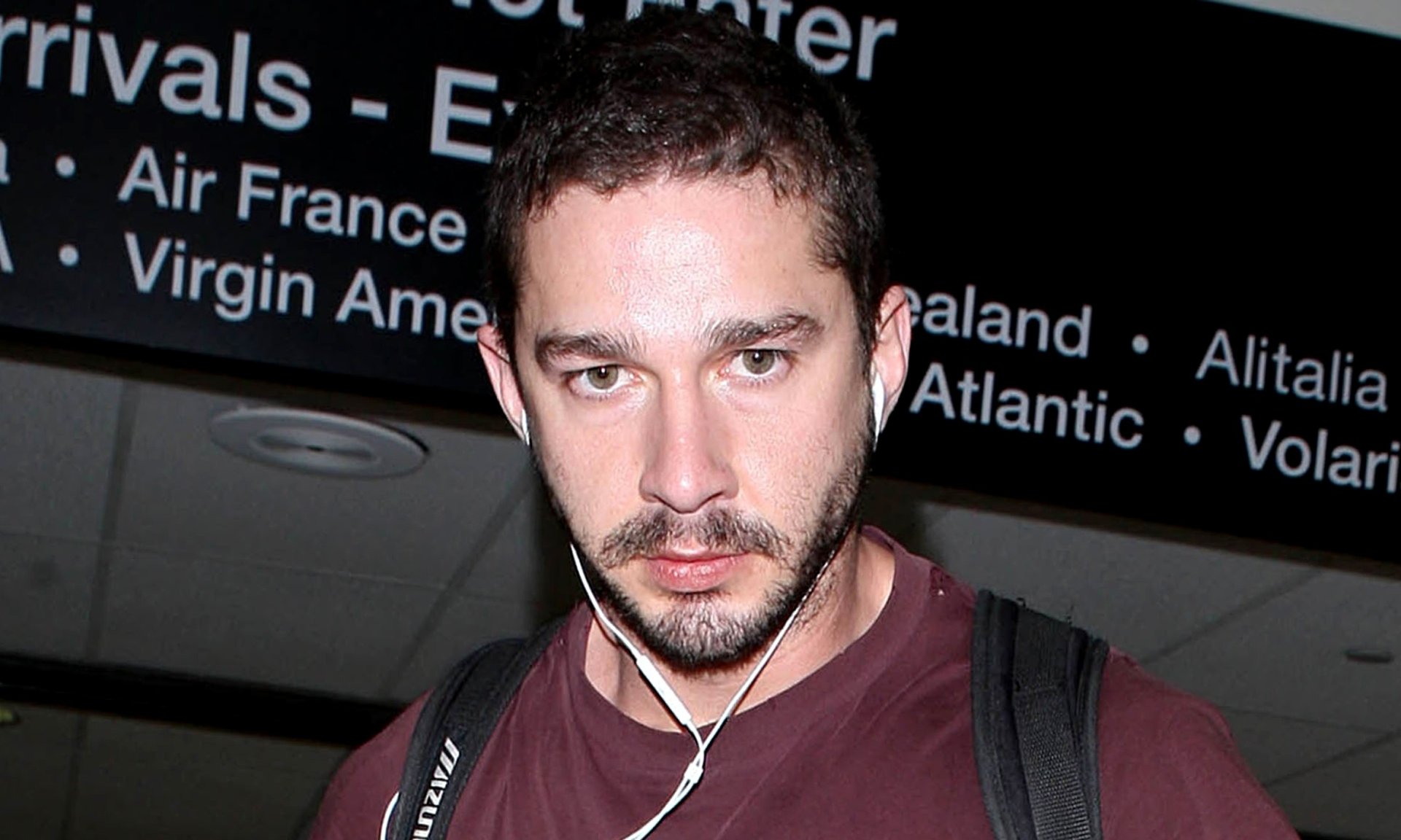 Shia LaBeouf captured in a candid moment at an airport, set as a high-definition desktop wallpaper.