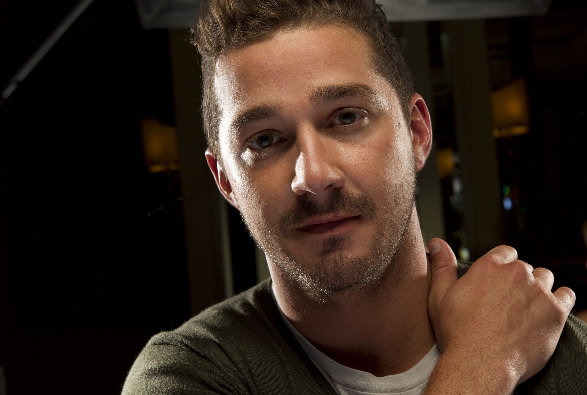 HD desktop wallpaper featuring a close-up of Shia LaBeouf with a subtle smile in a dimly lit setting.