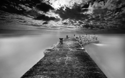 Black and white photography of a textured pier extending into calm water under a dramatic sky, captured in HD for a striking PC desktop wallpaper background.