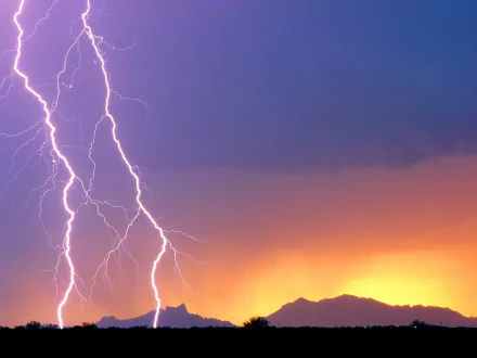 HD desktop wallpaper featuring vibrant lightning bolts striking over silhouetted mountains beneath a dramatic sky at sunset, showcasing nature's power and beauty.