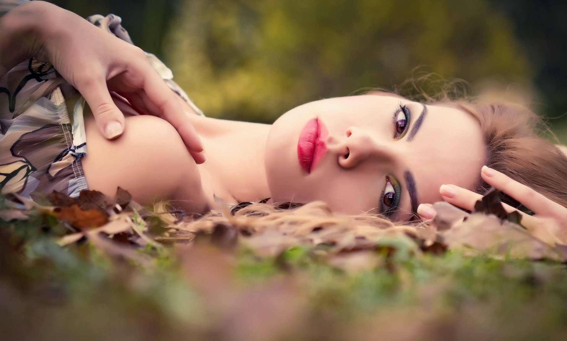 A serene fall scene featuring a woman with striking features resting among colorful leaves, capturing the essence of autumn in a high-definition wallpaper.
