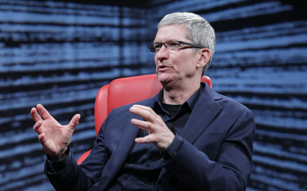 Tim Cook, the CEO of Apple, is seen in a black suit, gesturing expressively while seated in a red chair, set against a dynamic blue background, suitable as an HD desktop wallpaper.