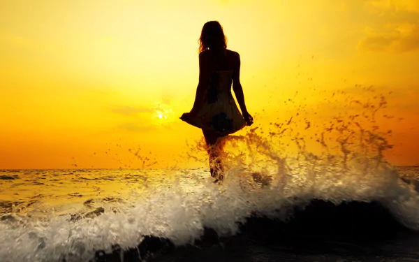 A serene sunset over the ocean, with a woman standing in the waves, creating a tranquil atmosphere. This HD wallpaper captures the beauty of nature and solitude.