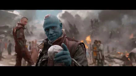 Yondu Udonta, portrayed by Michael Rooker, stands confidently in a chaotic scene from *Guardians of the Galaxy*, holding a glowing orb amidst the destruction.