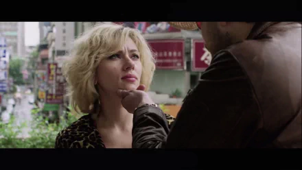 HD desktop wallpaper featuring Scarlett Johansson from the movie Lucy, capturing a tense moment between characters on a city street.