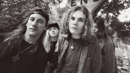 Black-and-white HD PC desktop wallpaper: moody close-up portrait of a 1990s alternative rock band under a street sign, capturing a grunge-era music aesthetic.