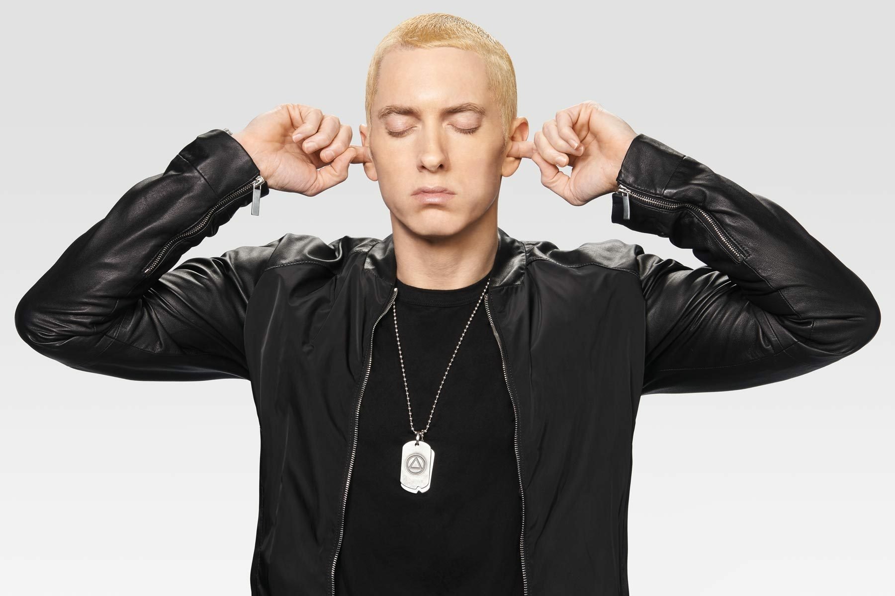 A high-definition desktop wallpaper featuring Eminem with his eyes closed and fingers in his ears, exuding a contemplative mood against a soft gray background.