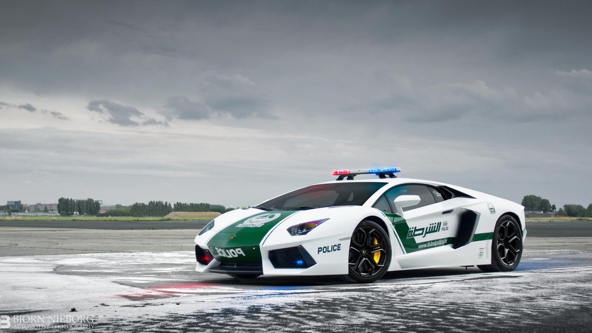 A striking Lamborghini Aventador police vehicle stands on a wet runway, showcasing its sleek design and vibrant colors, making for a captivating HD desktop wallpaper and background.