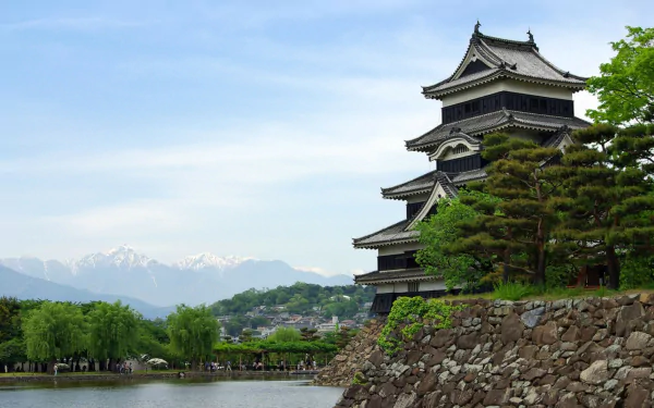 HD desktop wallpaper featuring Matsumoto Castle, a man-made historic structure in Japan, set against a backdrop of mountains and lush greenery.