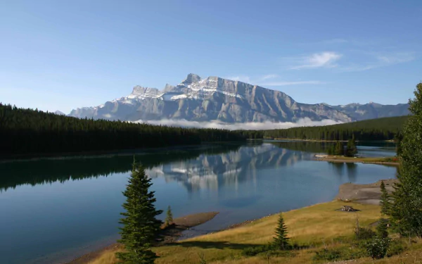 HD desktop wallpaper of Two Jack Lake showcasing calm waters, lush greenery, and a majestic mountain under a clear blue sky in a serene natural setting.