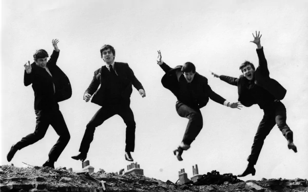 Black-and-white HD desktop wallpaper of The Beatles jumping in the air against a plain background, capturing their iconic energy and music legacy.