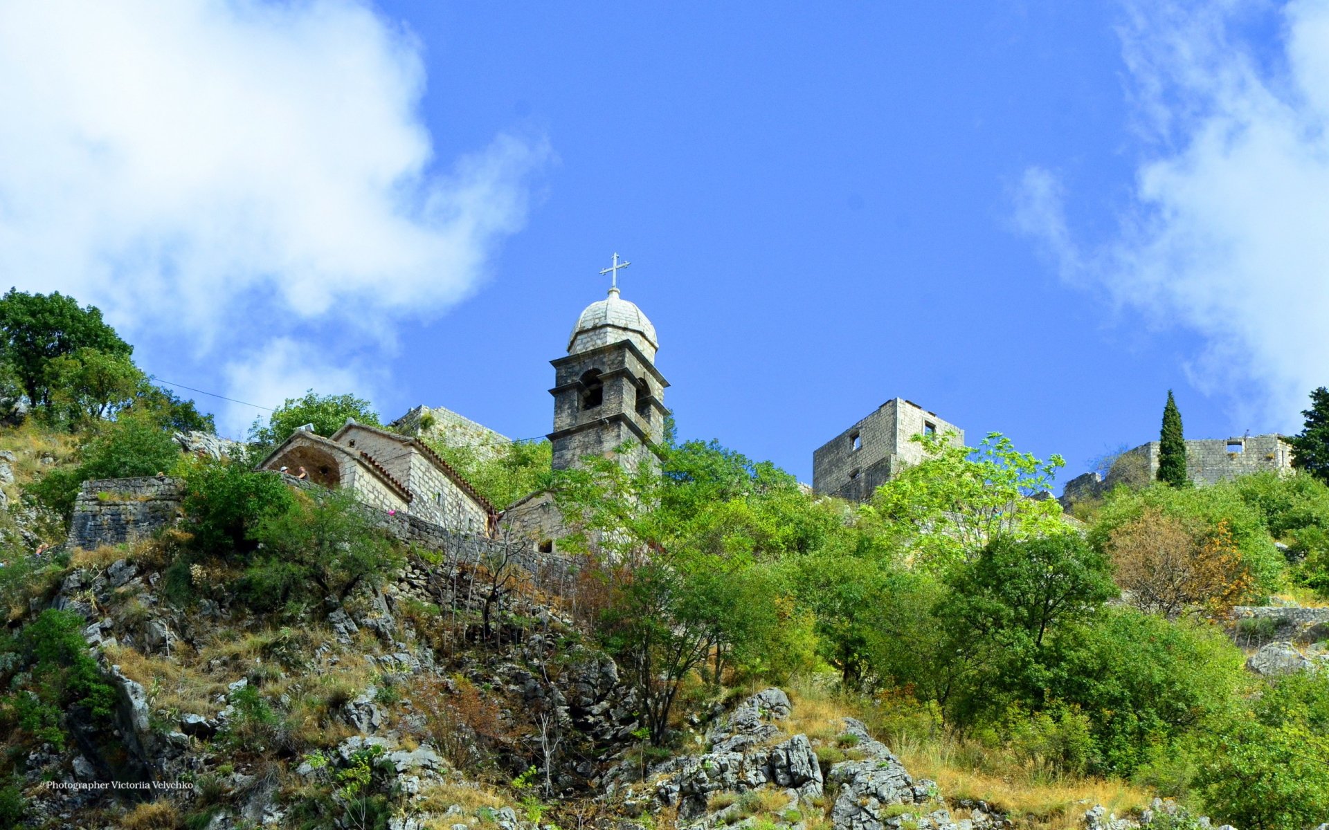 HD PC desktop wallpaper of a serene church perched on a rocky hillside under a bright blue sky, blending religious architecture with natural scenery.