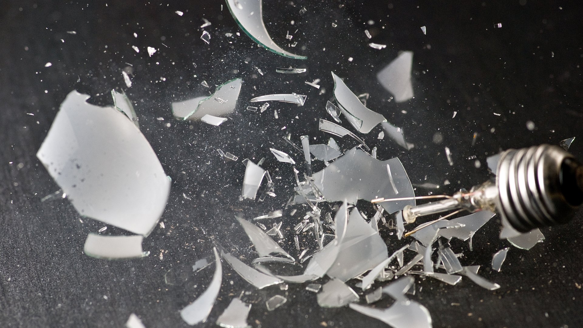 HD wallpaper of an exploding light bulb with shards of glass suspended in the air, creating a dynamic background.