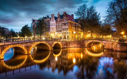 A beautifully illuminated Amsterdam scene featuring historic buildings and charming bridges reflecting on the water, captured as a stunning high-definition desktop wallpaper.
