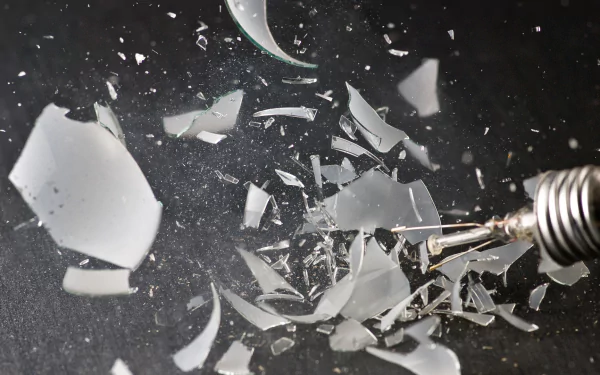 HD wallpaper of an exploding light bulb with shards of glass suspended in the air, creating a dynamic background.