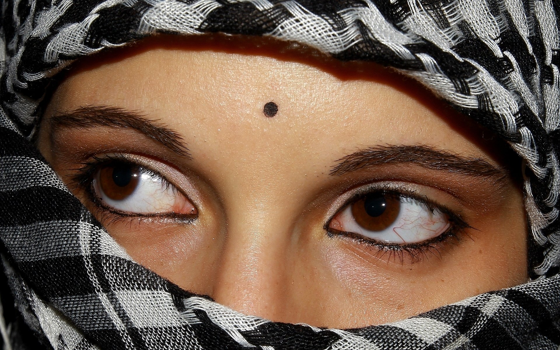 Close-up HD desktop wallpaper of a woman's intense brown eyes, partially covered by a black and white patterned scarf.