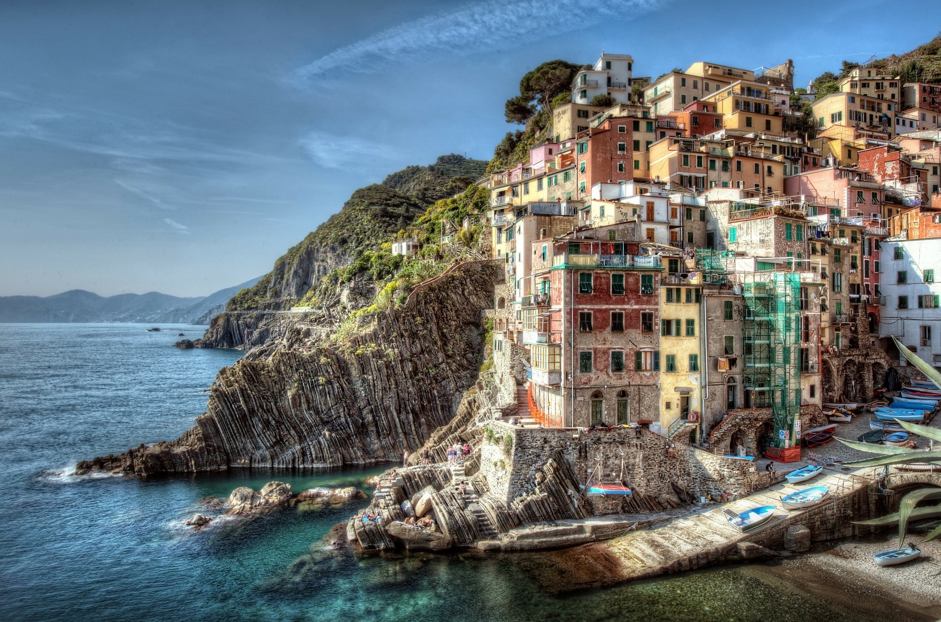 Colorful buildings of Riomaggiore in Cinque Terre, Liguria, Italy, perched on rocky cliffs overlooking the sea under a blue sky.