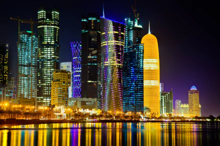 HD desktop wallpaper of Doha's night skyline, featuring illuminated modern skyscrapers reflecting on the water.