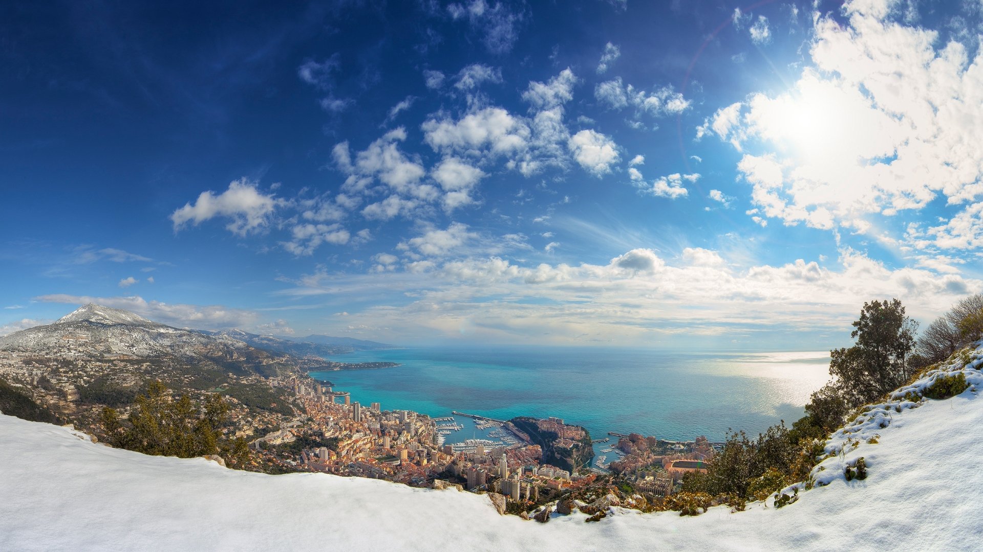 2K Quad HD PC desktop wallpaper and background: panoramic Monaco landscape — blue sky, turquoise sea, coastal cityscape and man-made harbor viewed from a snowy hillside.