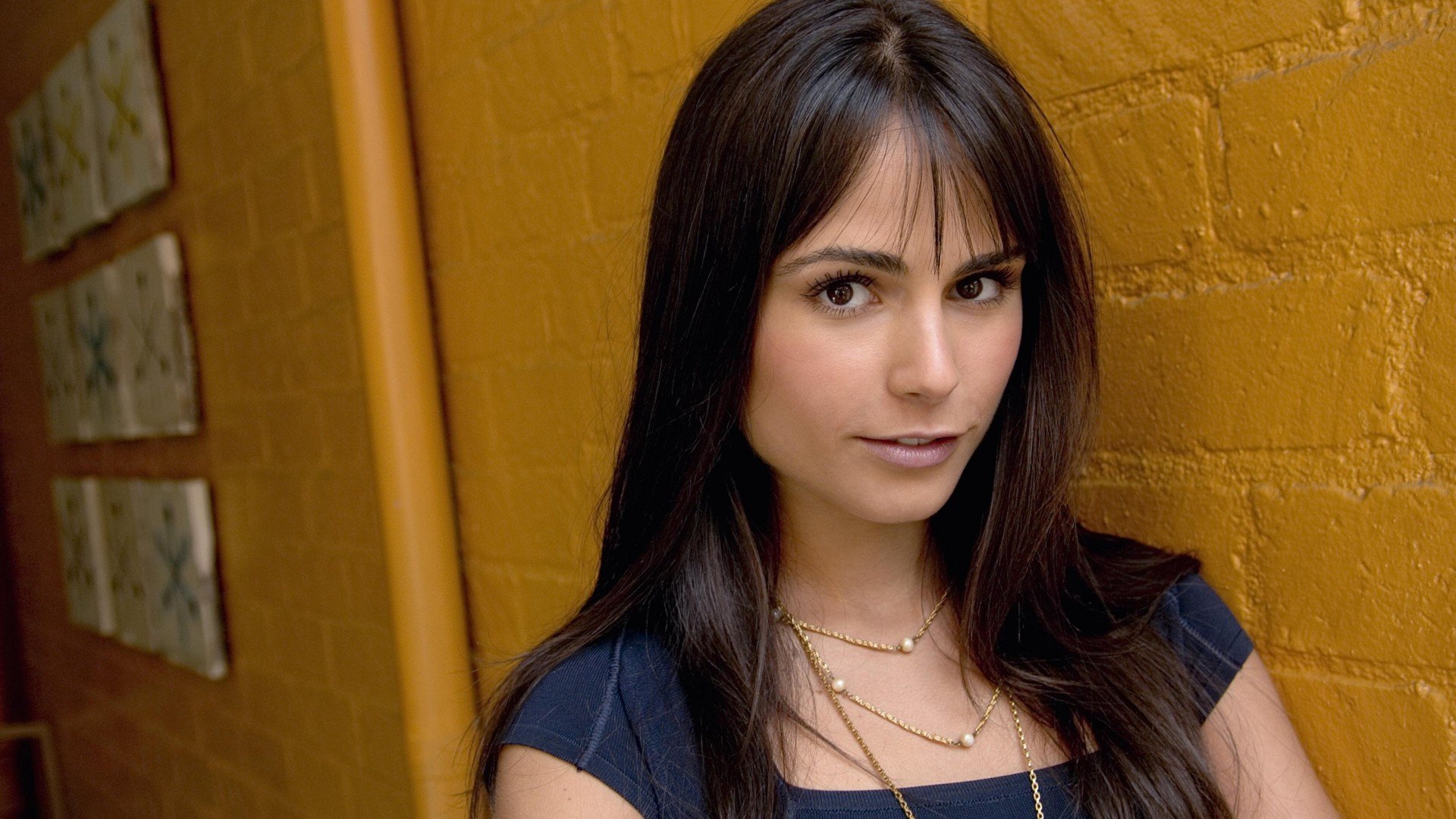 HD desktop wallpaper featuring Brazilian actress and celebrity Jordana Brewster against a textured yellow wall background.