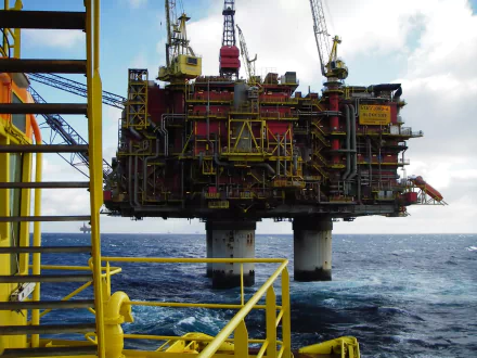HD PC desktop wallpaper and background showing a man-made offshore oil platform rising from the sea, seen from a yellow-railed walkway beneath a cloudy sky.