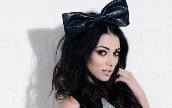 HD desktop wallpaper of a dark‑haired female model with dramatic makeup and a large black bow headband, posing against a white textured wall.